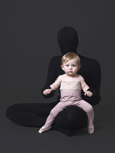 Baby girl models pink pyjamas with dark figure hidden in background.