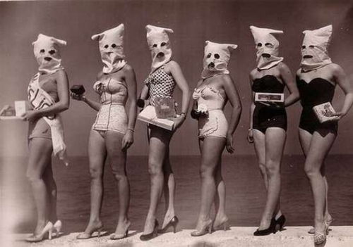Contestants pose on beach with creepy bags placed over their heads.