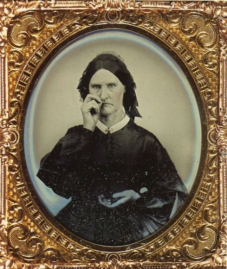 Photograph of a stern woman in black Victorian dress taking snuff, which looks very much like she is picking her nose.