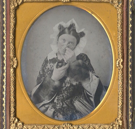 Photograph of a well-dressed Victorian lady taking snuff, which looks like she is picking fancy boogers out of her nose. 